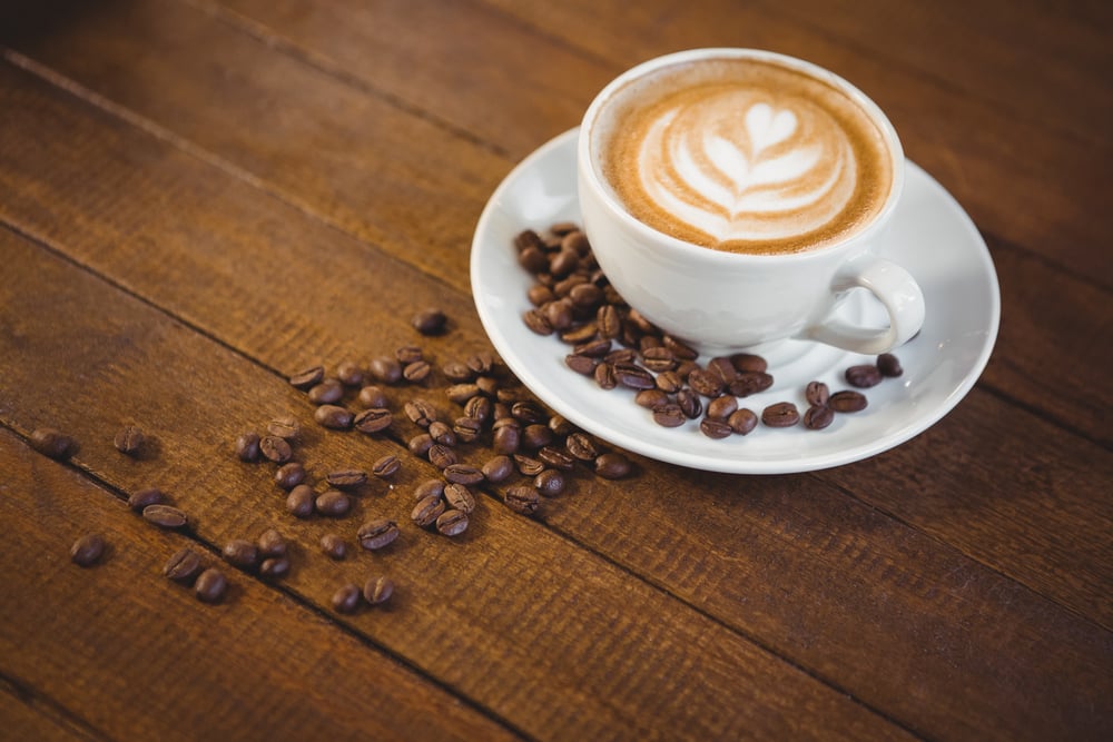 Cup of cappuccino with coffee art and coffee beans on wooden table